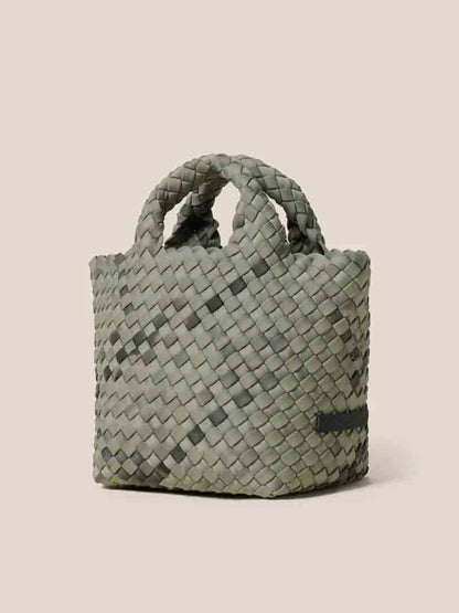 The Naghedi St. Barths Petit Tote in Watercolor Neptune is a small woven basket with handles, crafted from handwoven neoprene in a chic gray-green hue, elegantly set against a plain beige background.