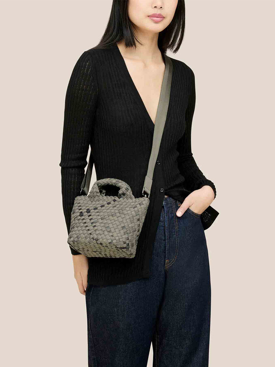 Person in a black ribbed cardigan and dark jeans, showcasing the Naghedi St. Barths Petit Tote in Watercolor Neptune with its elegant crossbody strap, while their right hand rests casually in their pocket.