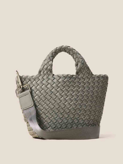 The Naghedi St. Barths Petit Tote in Solid Laurel is a small, gray handwoven neoprene handbag featuring handles and a detachable crossbody strap, elegantly set against a plain background.