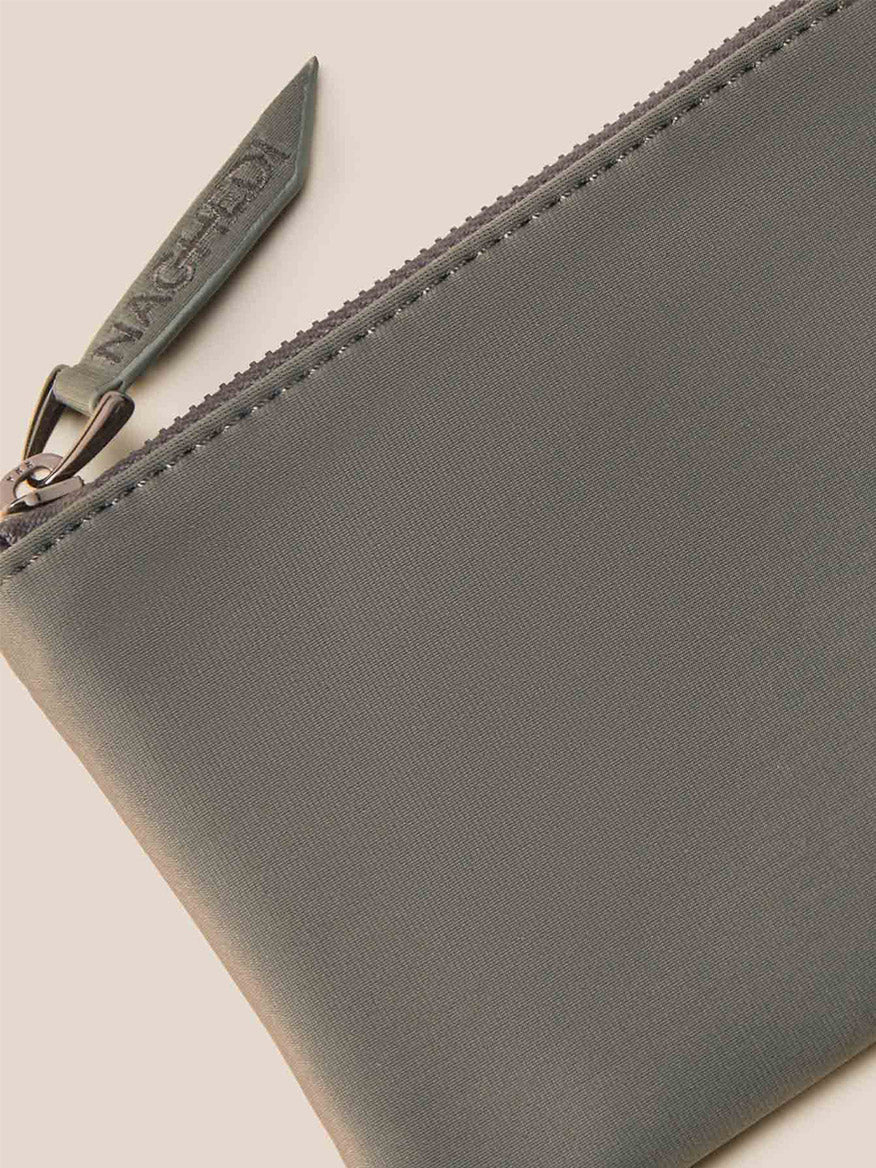 Experience the detail of the Naghedi St. Barths Petit Tote in Solid Laurel, featuring a close-up of its branded zipper pull on a gray pouch, elegantly complemented by a detachable crossbody strap.