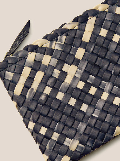 A detailed view of the Naghedi St. Barths Small Tote in Watercolor Nimbus reveals its handwoven neoprene surface with a captivating black and white checker pattern, complete with a charming zipper tag enhancing its appeal.
