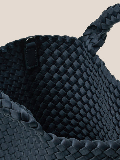 A close-up image of the Naghedi St. Barths Small Tote in Solid Murano, showcasing its dark, handwoven neoprene basket design with interlaced straps and a single handle, reminiscent of a petite tote.