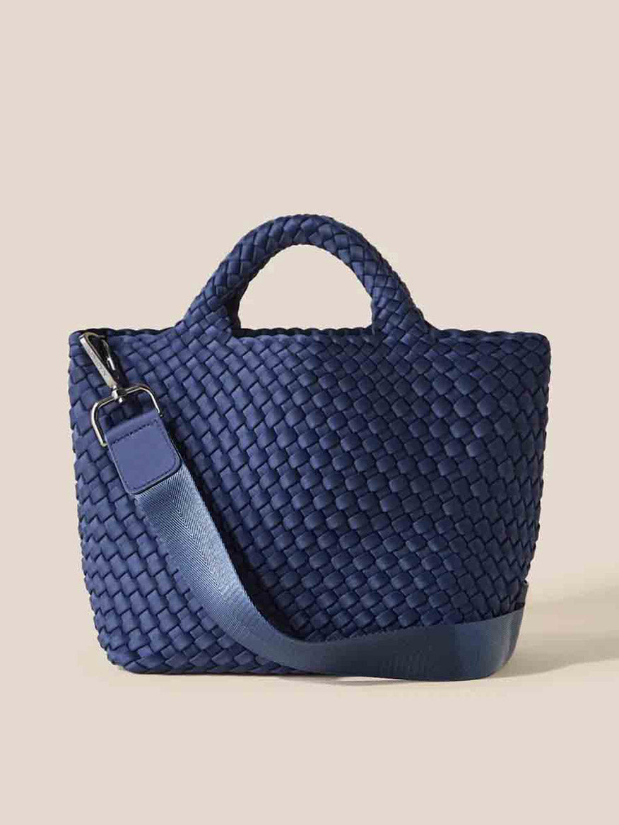 The Naghedi St. Barths Small Tote in Solid Ink Blue is made from handwoven neoprene and showcases a single handle and a detachable crossbody strap, elegantly displayed against a plain background.