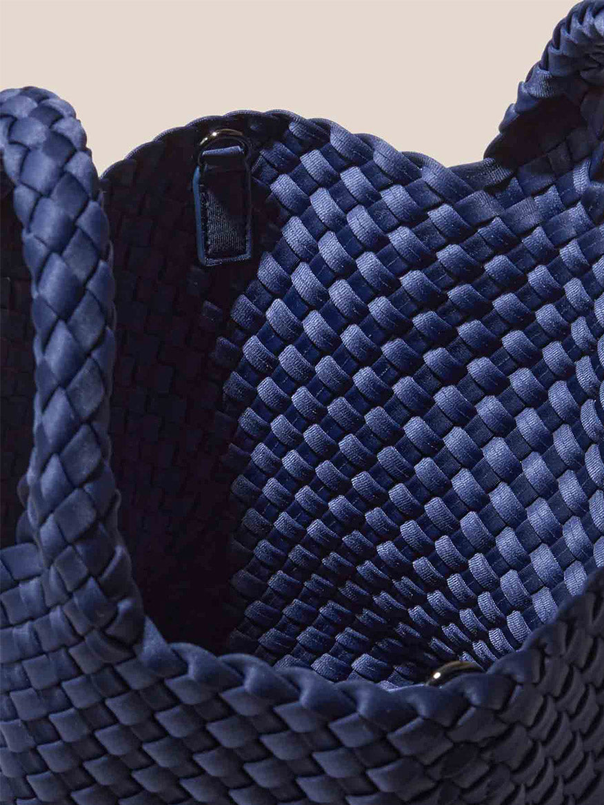 Close-up of the Naghedi St. Barths Small Tote in Solid Ink Blue, featuring a detailed interlaced pattern and open interior. This handwoven neoprene basket comes with handles and can also be used as a crossbody bag for added versatility.