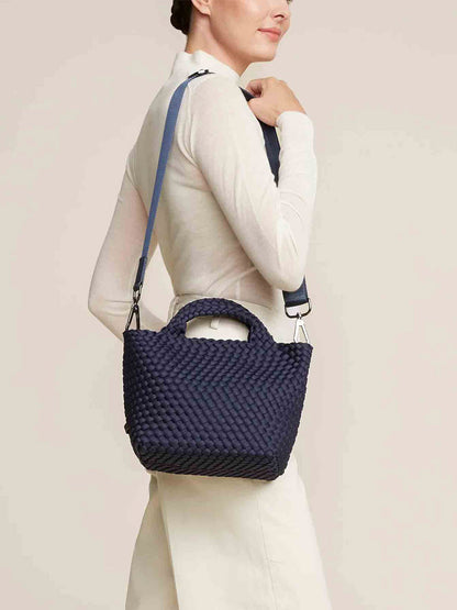 A person is holding a Naghedi St. Barths Small Tote in Solid Ink Blue, which perfectly complements their white outfit against a plain background.