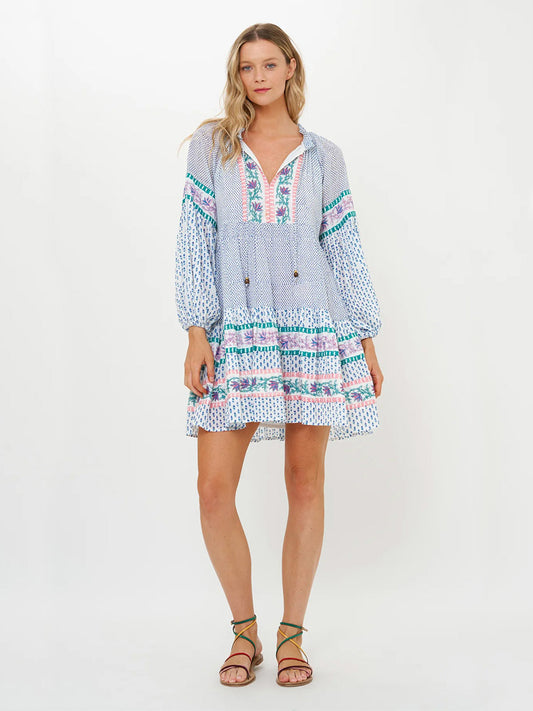 A woman models the Oliphant Balloon Sleeve Short Dress in Jungi Blue, crafted from lightweight cotton voile. The design features a blue and white pattern with pink and green accents using an exquisite block-printing technique on a plain background.