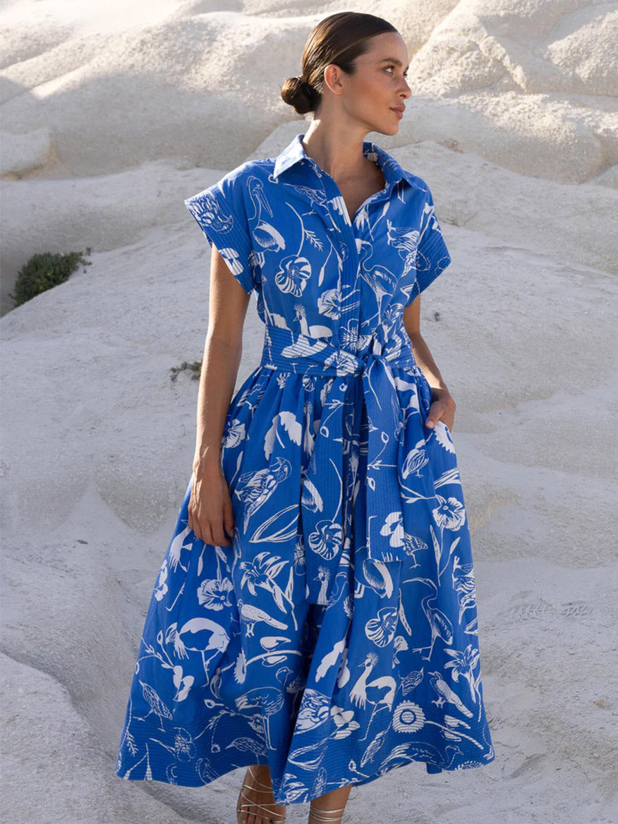 A woman in an Oliphant Belted Shirt Dress in Audubon Blue stands against a sandy background.