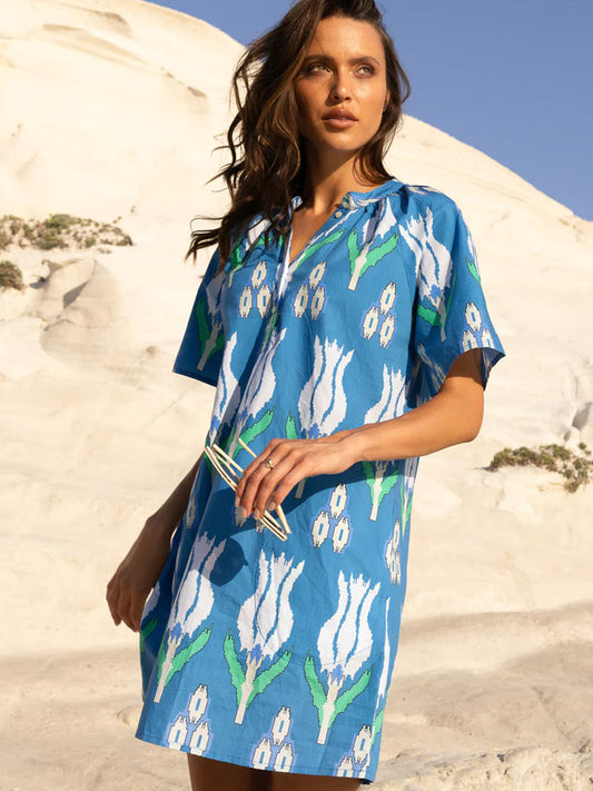Woman in a Oliphant Pocket Dress in Sumba Blue Tulip with button features and pockets standing against a sandy cliff background.