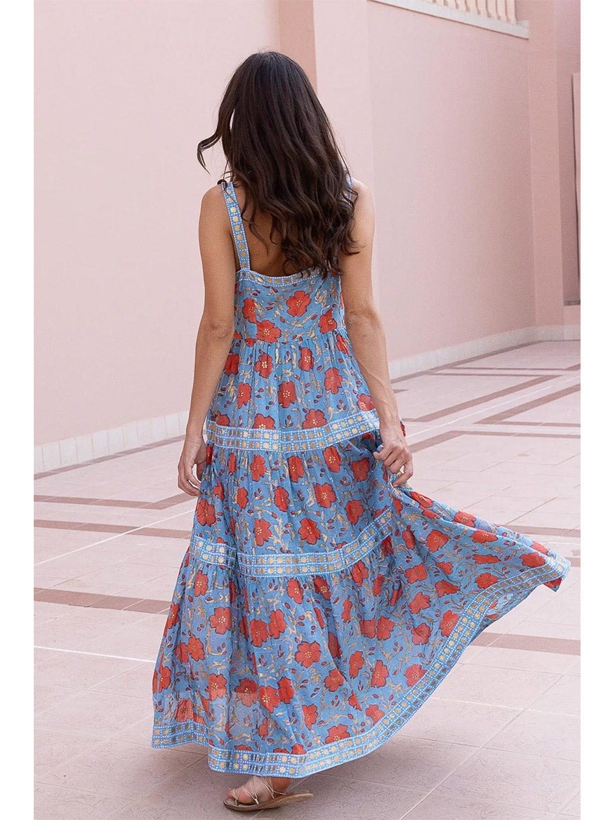 A woman in a Oliphant Strappy Maxi Dress in Poppy Red walks away, her hair flowing, in a pink corridor.