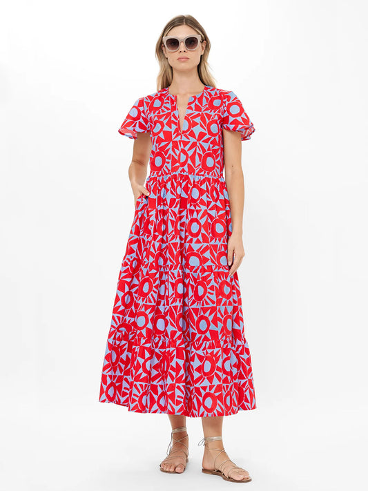 Woman in the Oliphant V-Neck Maxi Dress in Eclipse Red with flutter sleeves, sunglasses, and flat sandals, standing against a plain white background.