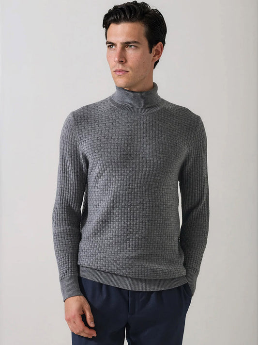 A man wearing the Patrick Assaraf Extra-Fine Merino Wool Basketweave Turtleneck in Castlerock and dark pants stands against a plain light background, looking to the side. The distinctive basketweave knit of this merino wool sweater adds visual interest and texture to his outfit.
