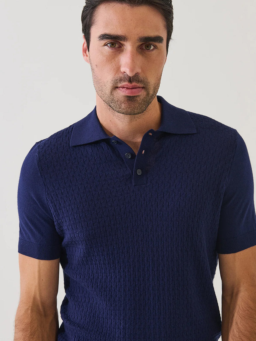 A man with short dark hair wears the Patrick Assaraf Cotton Blend Triangle Stitch Polo in Navy, featuring a subtle textured pattern, as he looks toward the camera against a plain light background.