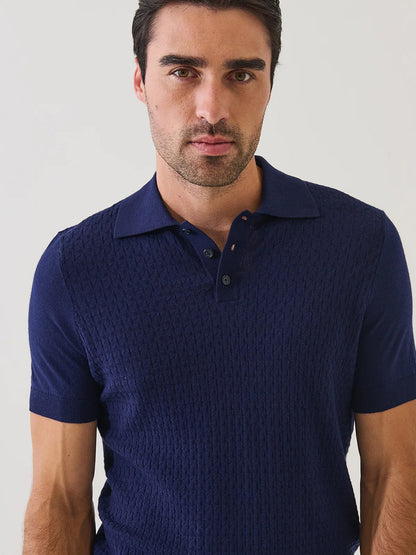 A man with short dark hair wears the Patrick Assaraf Cotton Blend Triangle Stitch Polo in Navy, featuring a subtle textured pattern, as he looks toward the camera against a plain light background.