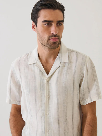 A man with dark hair wears the Patrick Assaraf Dobby Stripe Linen Camp Collar Shirt in Silver, a short-sleeve summer shirt with subtle vertical stripes, standing against a plain light background.