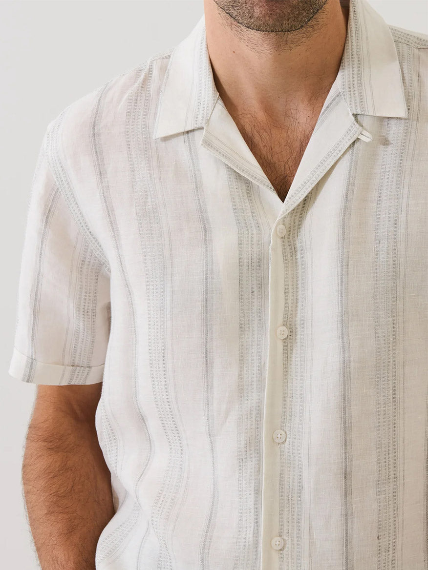 A man wears the Patrick Assaraf Dobby Stripe Linen Camp Collar Shirt in Silver, a short-sleeve white button-up with light gray vertical stripes, shown from shoulders to waist.
