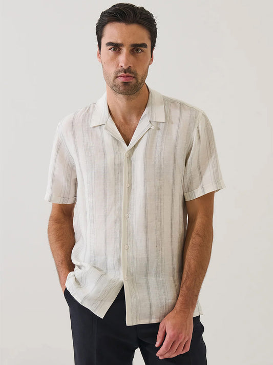 A man wears the Patrick Assaraf Dobby Stripe Linen Camp Collar Shirt in Silver with dark pants, standing against a plain light background.