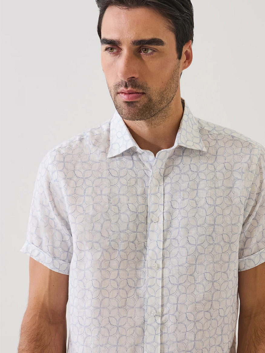 A man stands against a plain background, wearing the Patrick Assaraf Geometric Print Linen Shirt in Lake—a short-sleeve linen shirt with a subtle geometric print.
