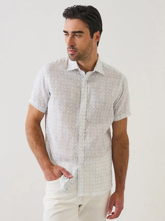 A man wears the Patrick Assaraf Geometric Print Linen Shirt in Lake with light pants, standing against a plain background.