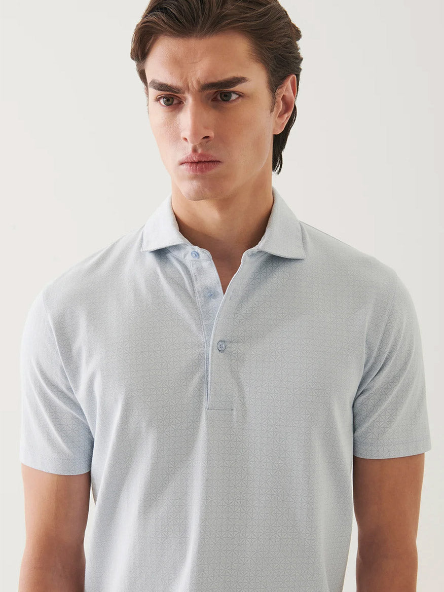 A young man with brown hair wears the Patrick Assaraf Pima Cotton Stretch Printed Polo in Blue Ice as he stands against a plain white background, looking slightly to the side with a neutral expression.