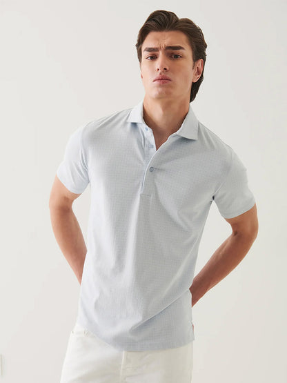 A young man wears the Patrick Assaraf Pima Cotton Stretch Printed Polo in Blue Ice with white pants, standing against a plain white background.