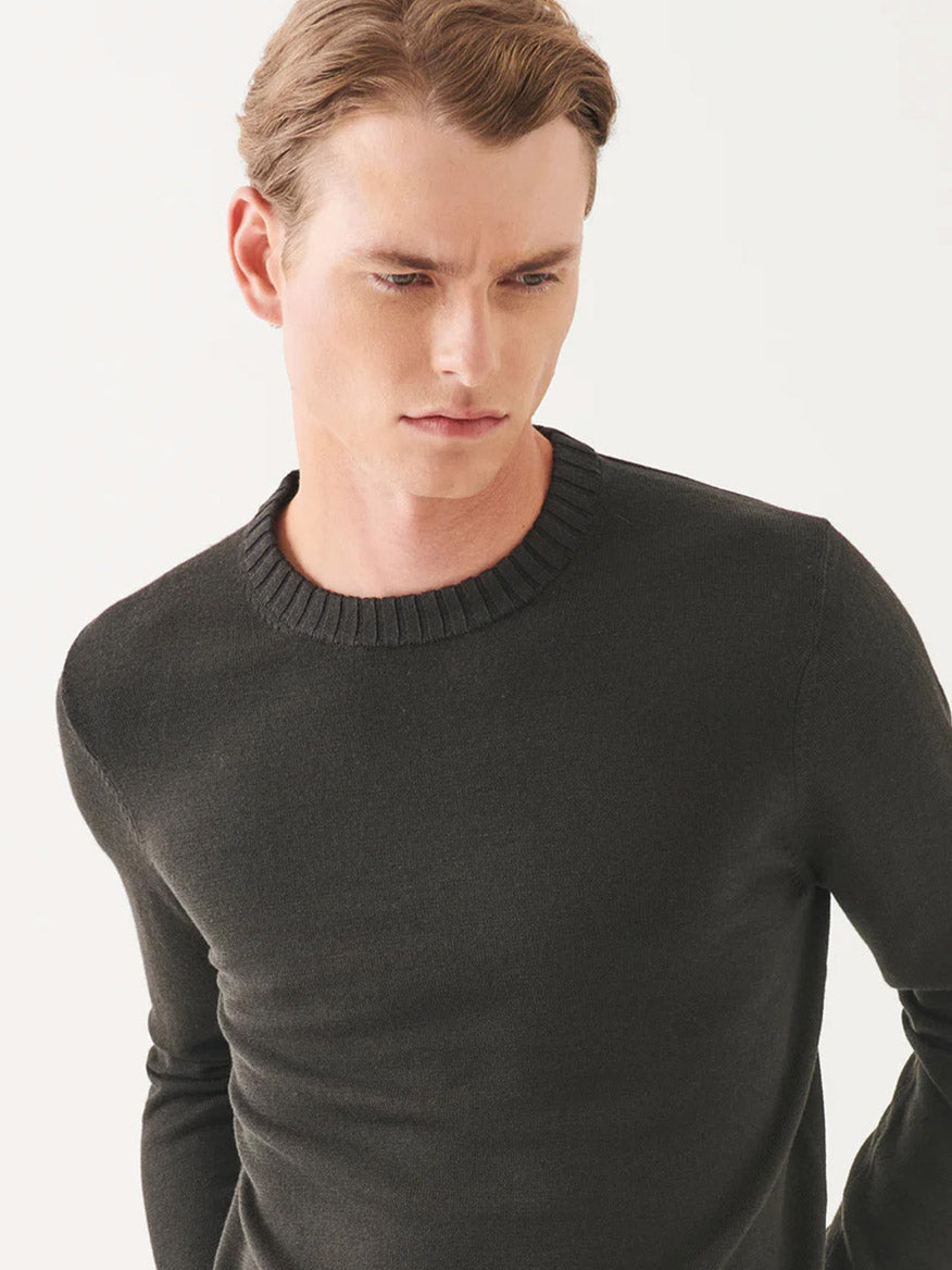 A person wearing the elegant form of a Patrick Assaraf Plaited Merino Wool Crewneck in dark brown gazes down against a plain white background.