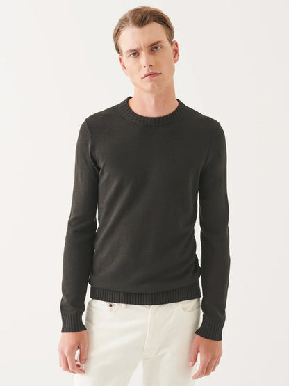 A person in a sleek silhouette featuring the Patrick Assaraf Plaited Merino Wool Crewneck in Dark Brown and white pants stands against a plain background.