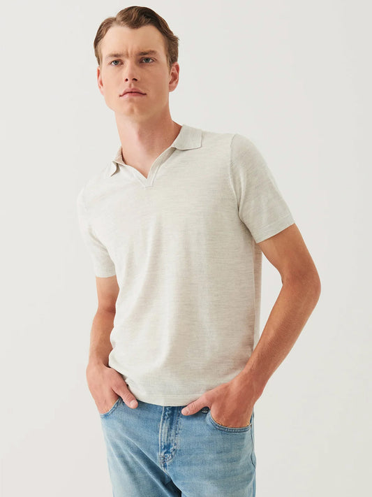 A man stands against a plain background wearing the Patrick Assaraf Cotton Cupro Open Polo in Drizzle and blue jeans, his hands in his pockets for versatile styling.
