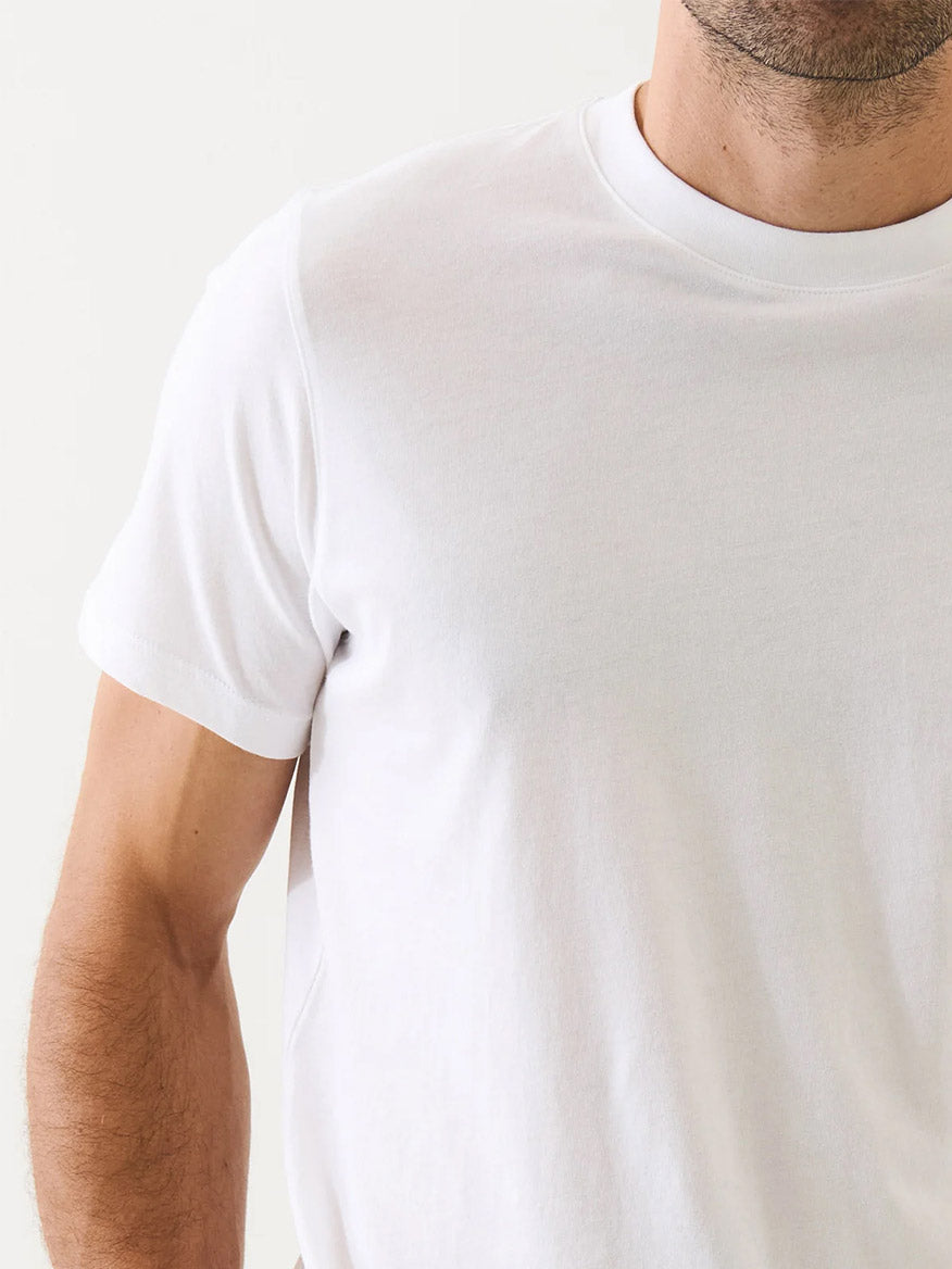 A man stands against a light background, visible from chest to neck, wearing the Patrick Assaraf Organic Pima Cotton High Neck T-Shirt in white.