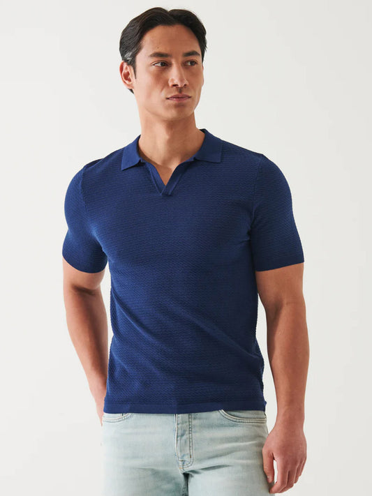 Man in a Patrick Assaraf Cotton Cupro Open Polo in Navy and light blue jeans standing against a white background.