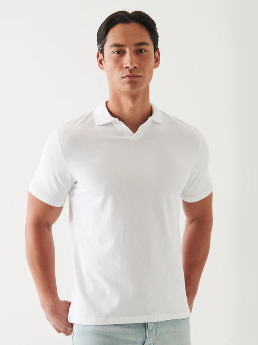 A man in a Patrick Assaraf Pima Cotton Stretch Open Polo in White stands against a plain background, looking directly at the camera with a neutral expression.