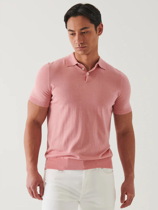 A man in a Patrick Assaraf Cotton Cupro Polo in Guava and white pants, looking downward with a neutral expression against a plain background.