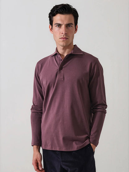 A man wearing the Patrick Assaraf Pima Cotton Stretch Long Sleeve Polo in Prune and dark pants stands against a plain light background with a neutral expression.