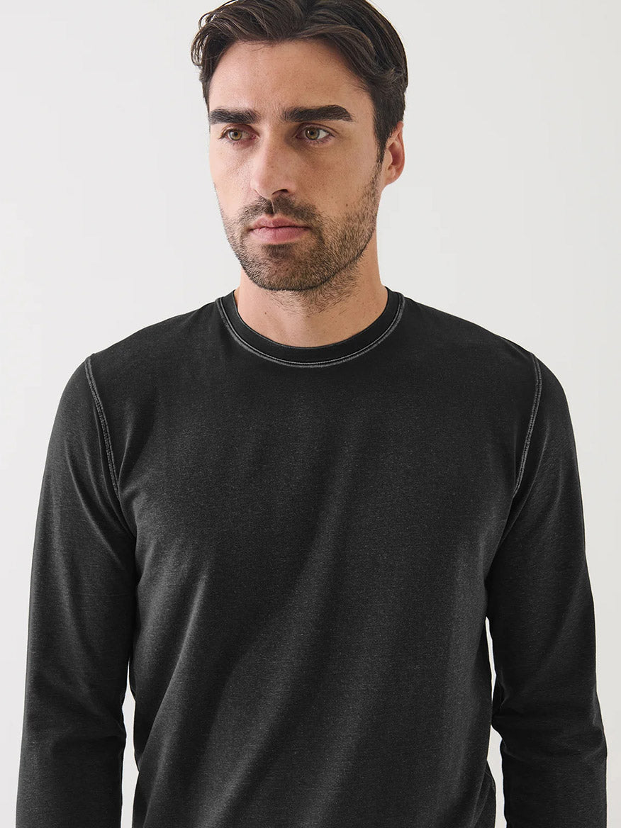 A man with short brown hair and a beard wears the Patrick Assaraf Pima Cotton Stretch Vintage Wash Long Sleeve T-Shirt in Black, crafted from luxurious Peruvian pima cotton with a soft vintage finish, as he stands against a plain white background.