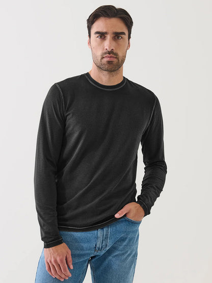 A man wearing the Patrick Assaraf Pima Cotton Stretch Vintage Wash Long Sleeve T-Shirt in Black and blue jeans stands against a plain white background, looking directly at the camera with a neutral expression.
