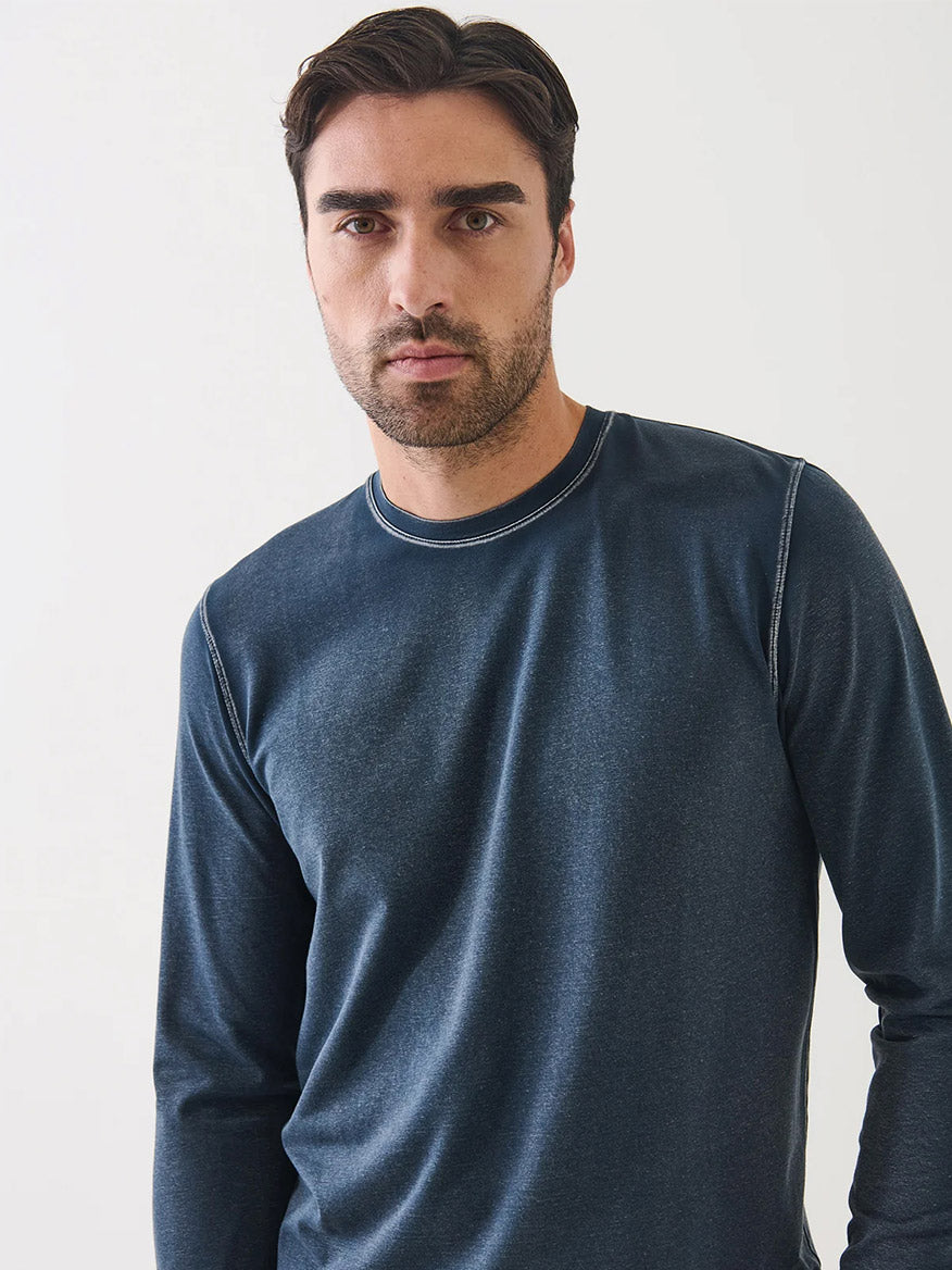 A man with short dark hair and a trimmed beard wears the Patrick Assaraf Pima Cotton Stretch Vintage Wash Long Sleeve T-Shirt in Midnight, made from soft Peruvian pima cotton, standing against a plain light background.