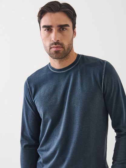 A man with short dark hair and a trimmed beard wears the Patrick Assaraf Pima Cotton Stretch Vintage Wash Long Sleeve T-Shirt in Midnight, made from soft Peruvian pima cotton, standing against a plain light background.