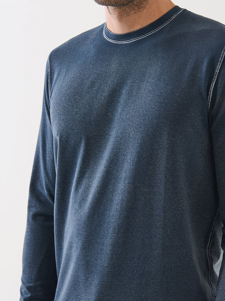 A person wearing the Patrick Assaraf Pima Cotton Stretch Vintage Wash Long Sleeve T-Shirt in Midnight, featuring visible stitching and crafted from luxurious Peruvian pima cotton; only the torso and lower face are shown against a plain background.