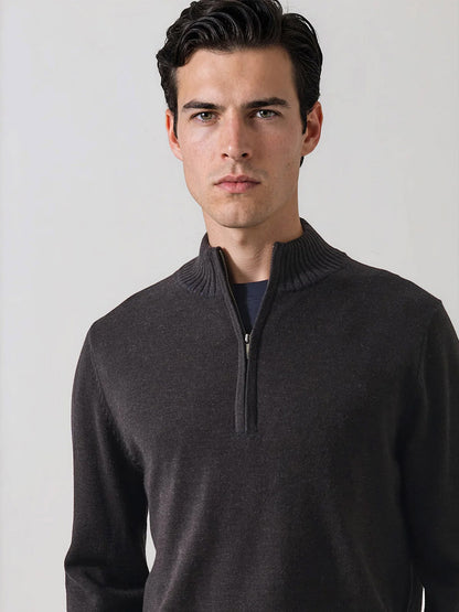 A man with short dark hair wears the Patrick Assaraf Merino Plaited Quarter Zip in Brownie, standing against a plain light background and facing the camera with a neutral expression. The refined silhouette of the brown sweater delivers lightweight warmth while maintaining a modern, polished look.