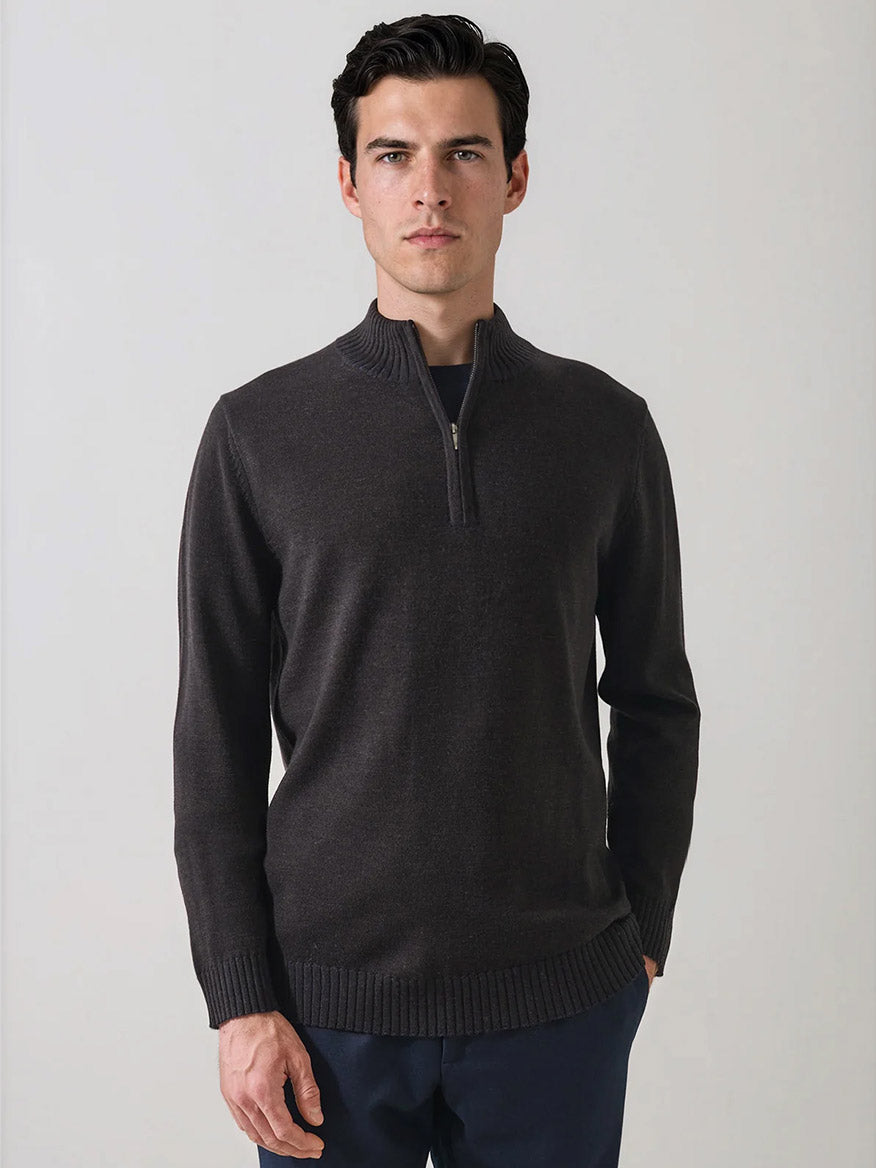 A man stands facing forward, wearing the Patrick Assaraf Merino Plaited Quarter Zip in Brownie and dark pants against a plain, light-colored background. The refined silhouette of his outfit offers lightweight warmth with understated style.
