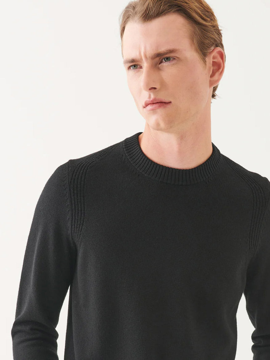 A person wearing the Patrick Assaraf Merino Crewneck in Black gazes to the side against a plain background, highlighting this ideal staple for any fall wardrobe.