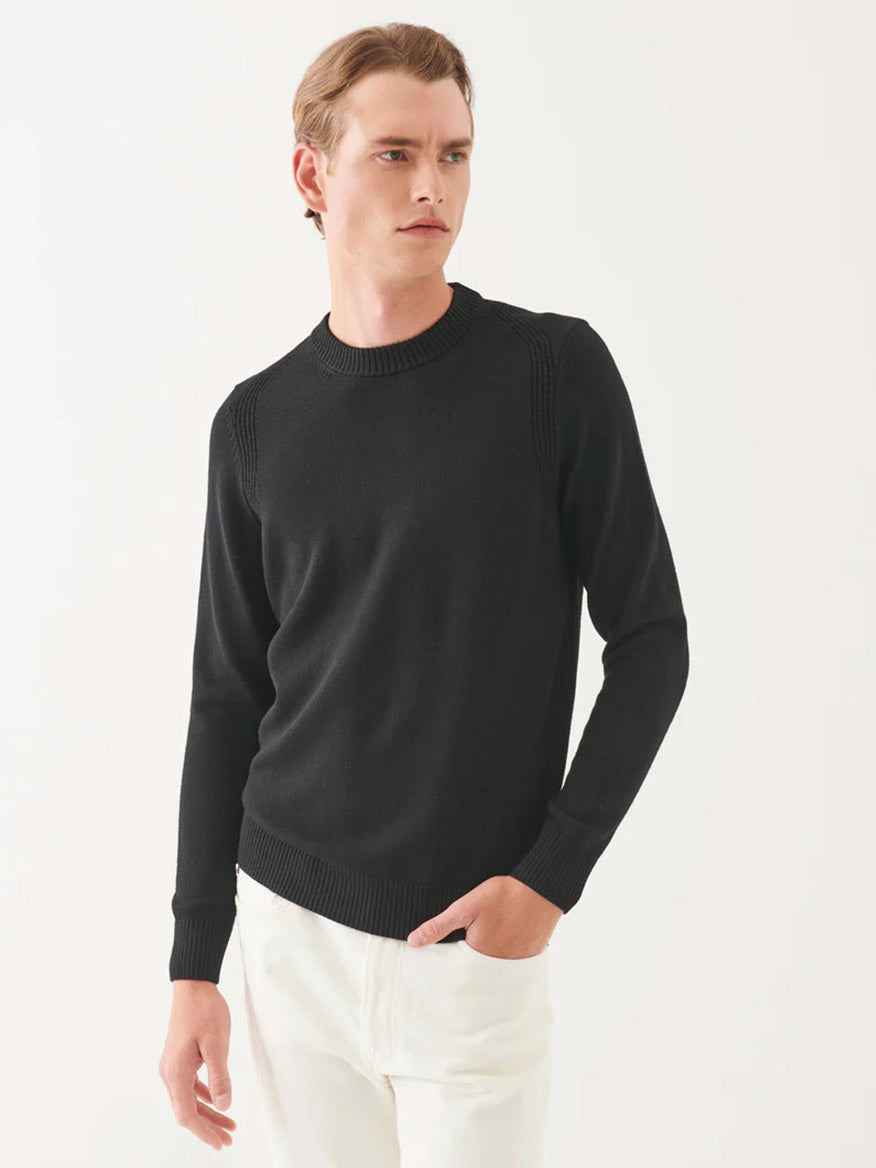 Person wearing the Patrick Assaraf Merino Crewneck in black, paired with white pants, standing against a white background.