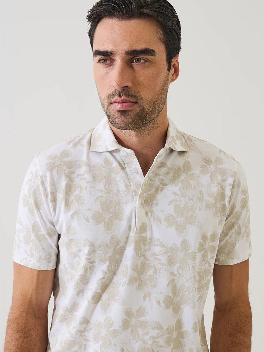 Man wearing the Patrick Assaraf Pima Cotton Stretch Tropical Print Polo in Frappe, featuring a light beige tropical motif, standing against a plain light background.