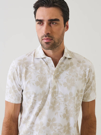 Man wearing the Patrick Assaraf Pima Cotton Stretch Tropical Print Polo in Frappe, featuring a light beige tropical motif, standing against a plain light background.