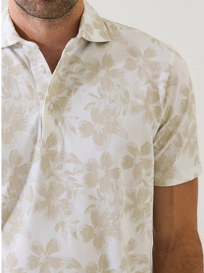 A person wearing the Patrick Assaraf Pima Cotton Stretch Tropical Print Polo in Frappe, showcasing its subtle beige tropical motif. Only their lower face, neck, and upper torso are visible.