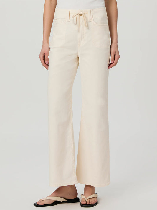 A person is wearing the Paige Ari Wide Leg Pant in Quartz Sand, tied at the waist with a drawstring, along with black flip-flops.