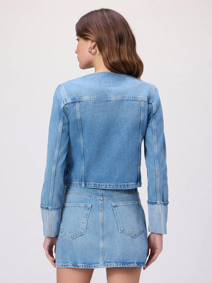 A woman stands with her back to the camera, wearing the Paige Dean Jacket in Del Amo—a light wash, collarless denim jacket—paired with a matching denim skirt, set against a plain background.