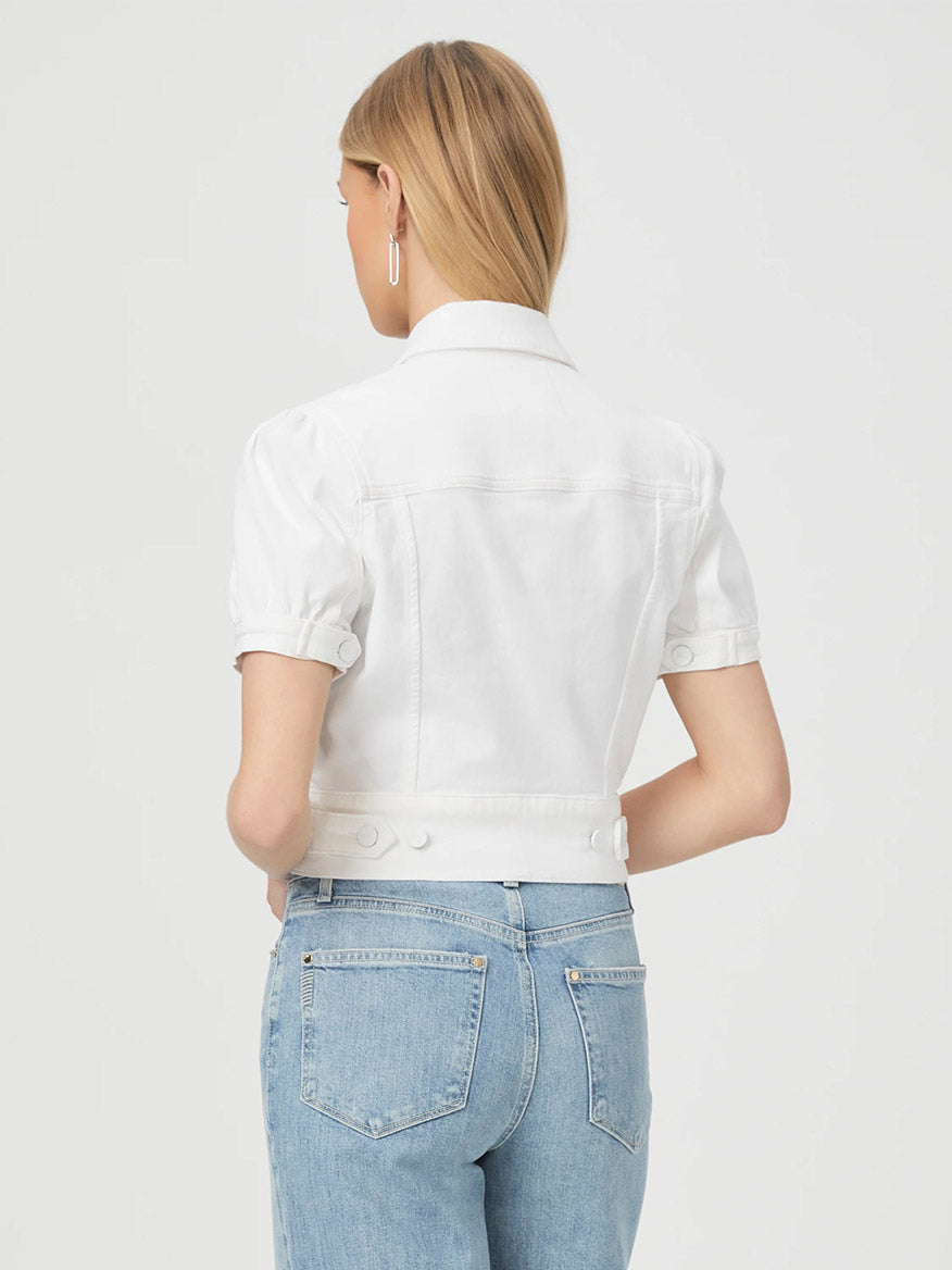 The image features an individual from behind, dressed in the Paige Kendra Jacket in Crisp White with blue jeans, set against a plain background.