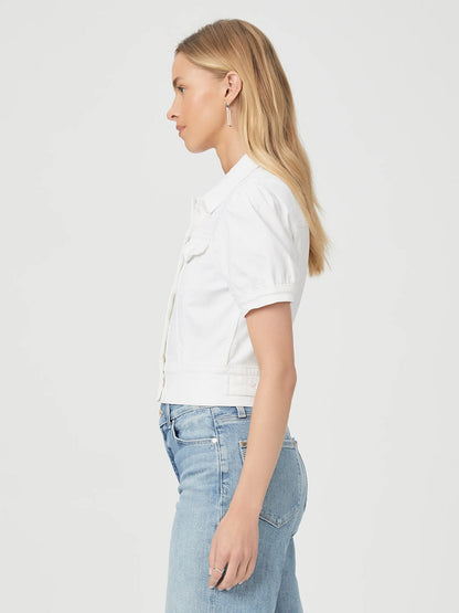 A woman with long blonde hair is shown in profile, wearing the Paige Kendra Jacket in Crisp White and blue jeans, against a neutral background.