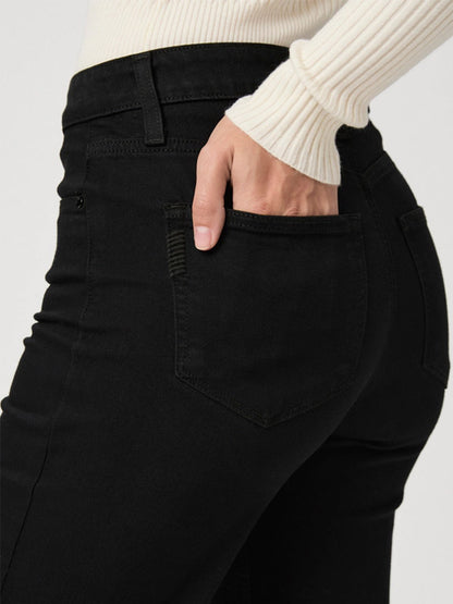 A person wearing Paige Leenah 32" Wide Leg Jean in Black Shadow and a white sweater is seen from the waist down, placing their hand in the back pocket of their pants.