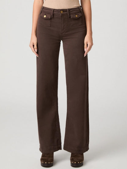 A person wearing the Paige Leenah 32″ Wide Leg Jean in Rich Chocolate, featuring utility patch pockets and gold buttons, paired with a beige top and brown platform shoes, stands against a plain background.